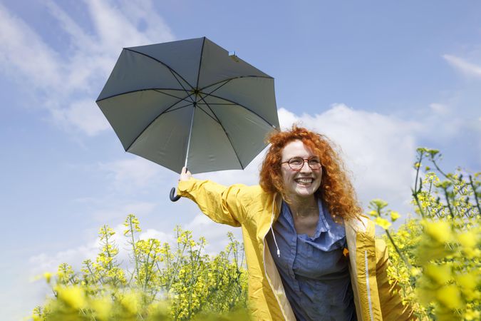 Red haired woman holding umbrella in yellow field