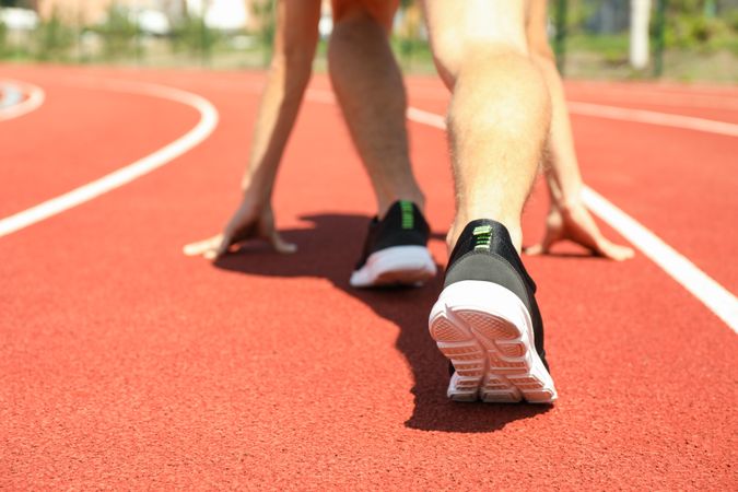 Sportsman low starting to run on red athletic track, close up