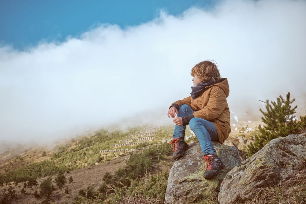 Boy in warm clothes observing nature from boulder