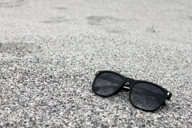 Sunglasses sitting on grey sandy pebbles