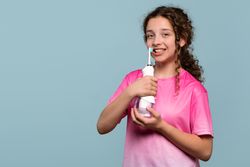 Young girl smiling, using electric toothbrush