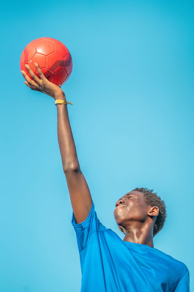 Black teenager with football ball against sky