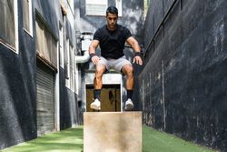 Concentrated athlete jumping on wooden box