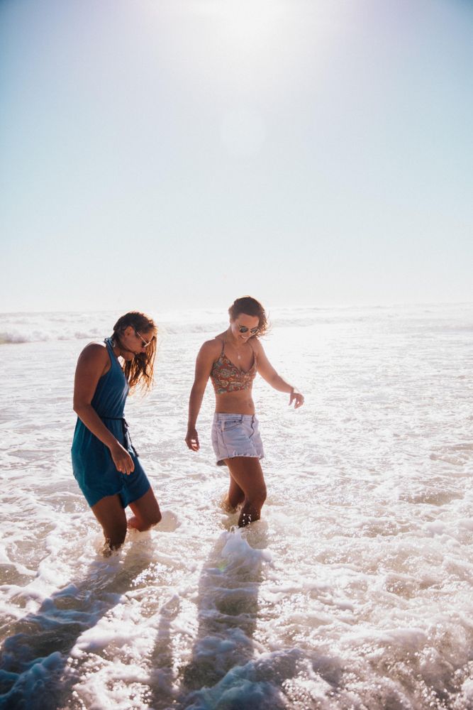 Two young women walk at the edge of the water at the beach