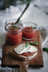Slice of fresh bread with cheese near tomatoes jam on cutting board