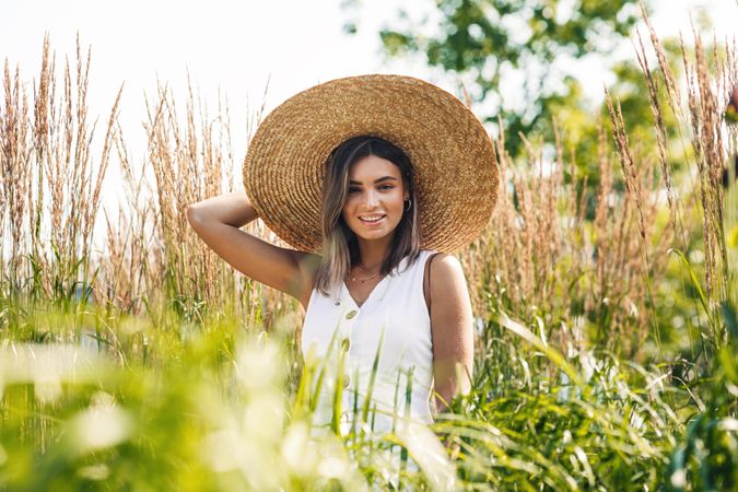 Smiling woman in straw hat standing outside in pond grass