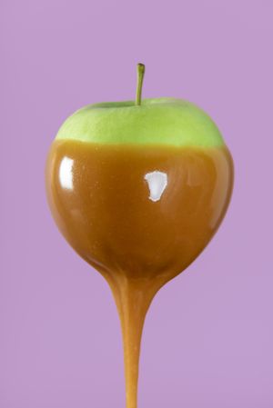 Green apple with caramel sauce close-up minimalist on purple background