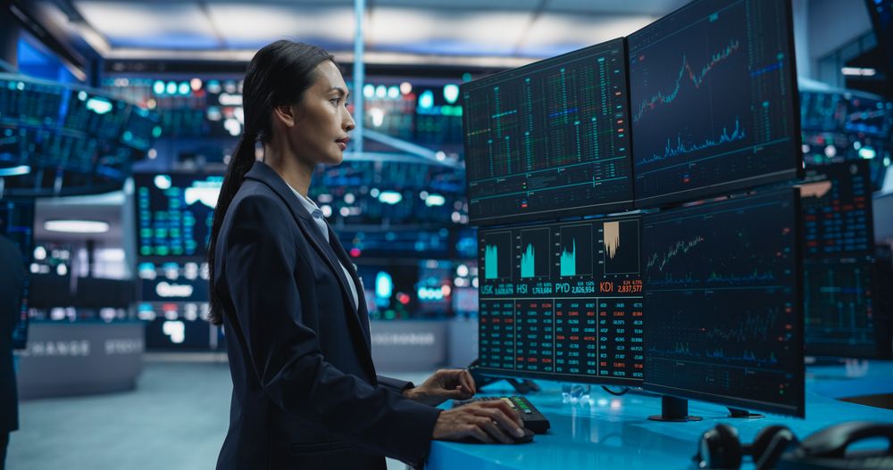 Young Female Stock Exchange Broker Working on Computer with Multi-Screen Workstation with Real-Time Stocks, Commodities and Exchange Market Charts.