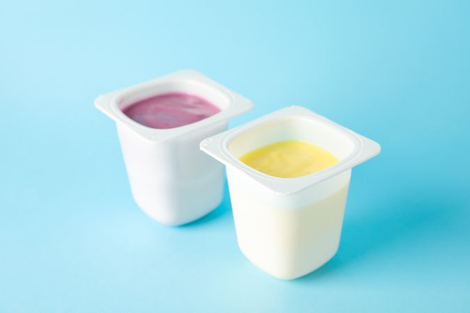 Plastic cups with yogurt on color background, space for text