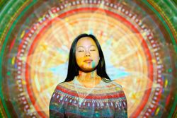 Peaceful Asian woman doing yoga near glowing mandala