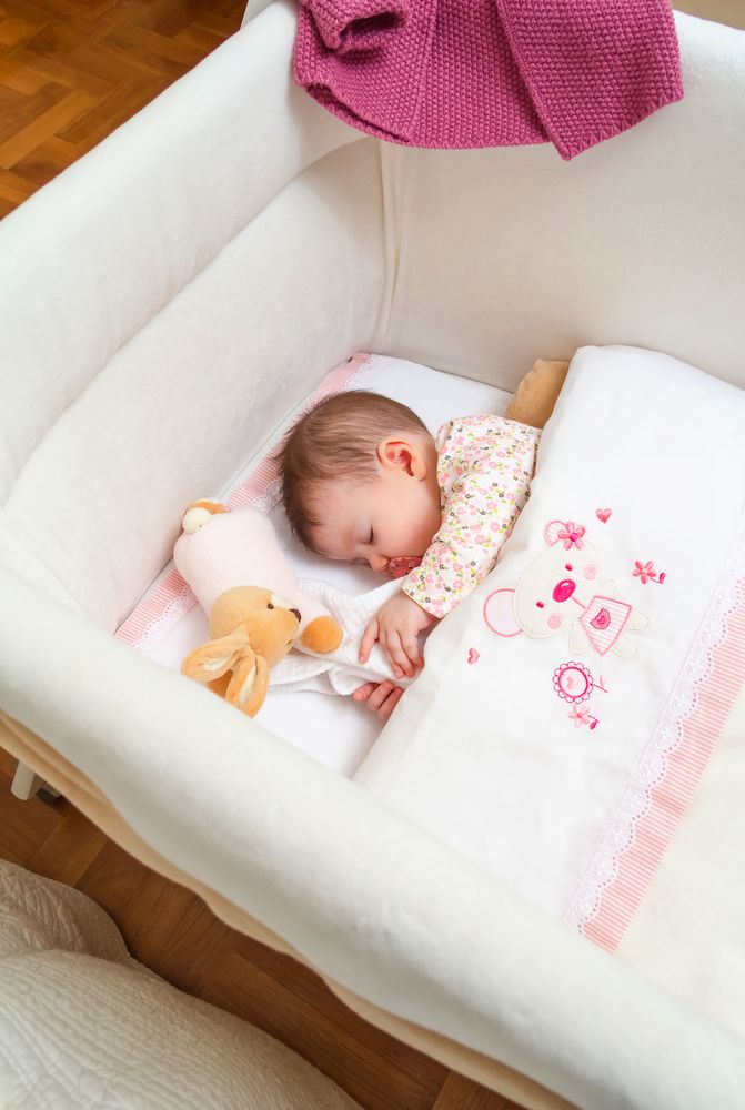 Baby girl sleeping in a white cot with pacifier and toy