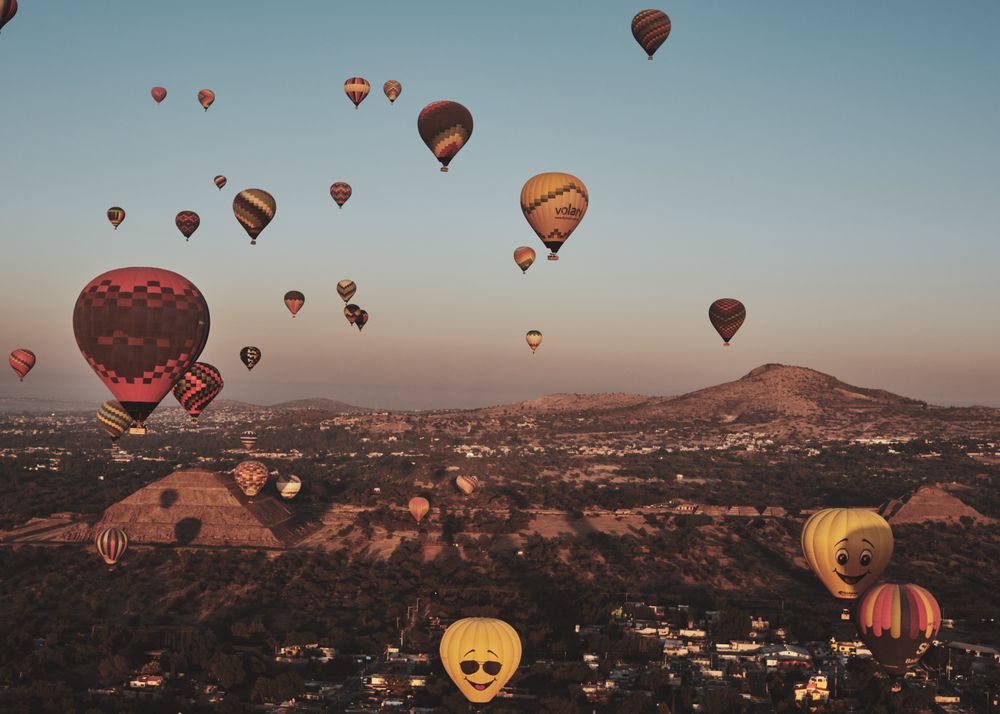 Many hot air balloons in flight over pyramids in Teotihuacan Valley