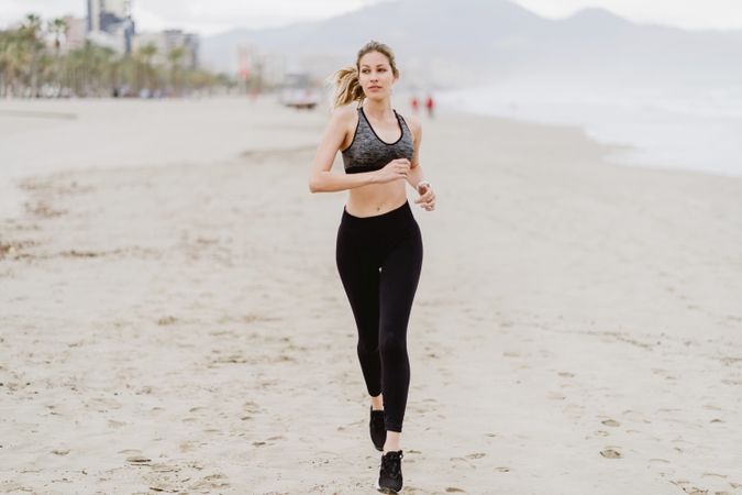 Female runner in stylish sportswear jogging along calm sandy seaside