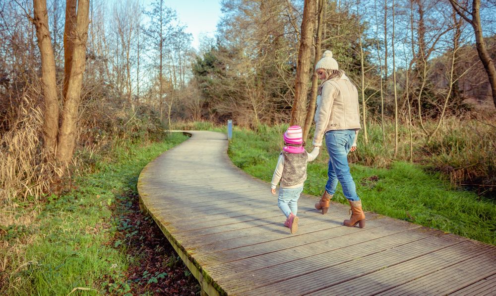 Mother and young daughter walking along trail in forest