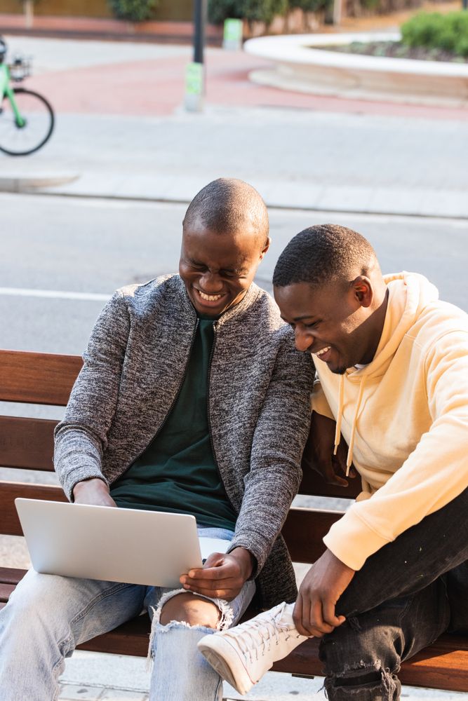 Smiling Black men using laptop while sitting on bench