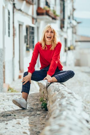 Laughing blonde female with red shirt sitting outdoors, vertical