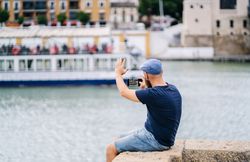 Guy on vacation in casual clothing making photo of bay on smartphone at quay