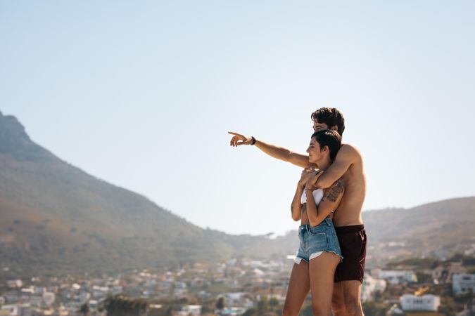 Couple standing on a hilltop and looking at the city down the hill