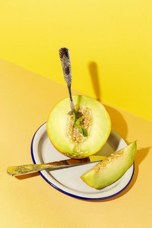 Sliced small melon on plate with spoon and fork