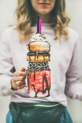 Woman holding stacked donut milkshake with straws, whipped cream, and chocolate sprinkles