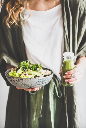 Woman in green cardigan standing holding vegetarian bowl and green smoothie