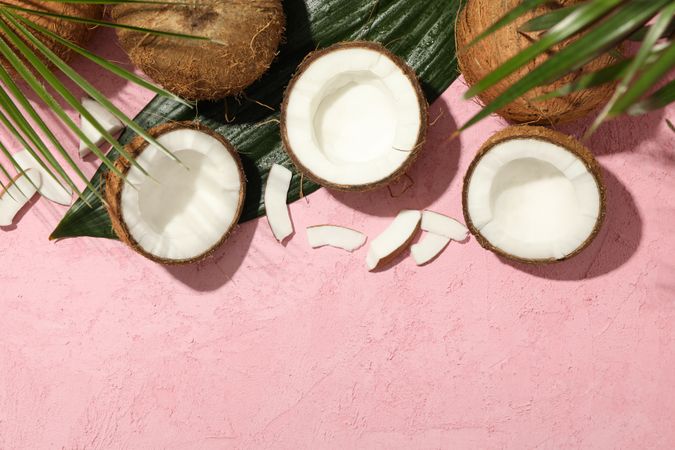 Coconut and palm leaves on pink background, top view