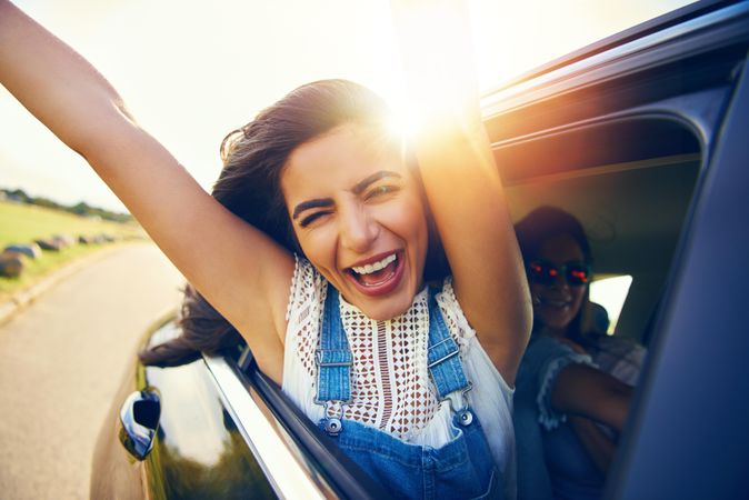 Smiling woman with arms outstretched outside of car window