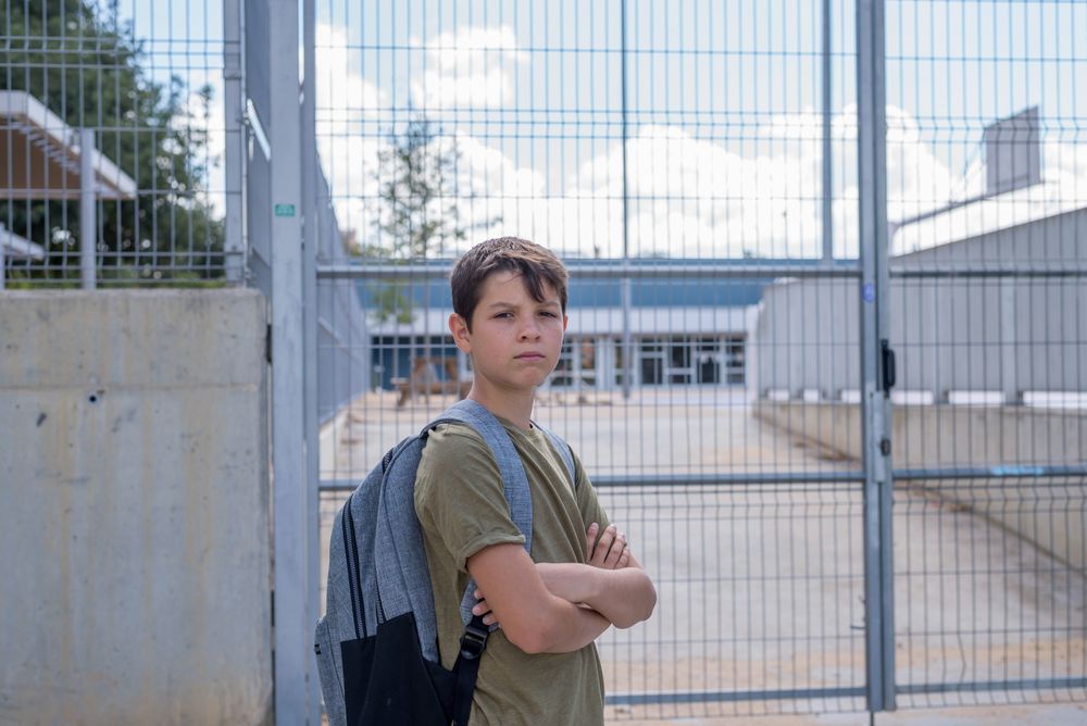Serious teenager in backpack smiling outside school gate