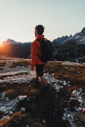 Back view of man in red jacket with backpack hiking in the mountains at sunset 428910