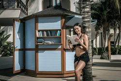 Smiling woman in dark bikini reading a book and leaning on a palm tree