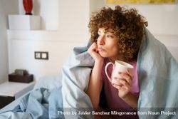Happy woman relaxing under blue sheet in bed with cup of coffee 5rm3P0