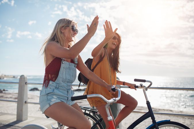 Two women on beach cruisers  on a summer day and giving each other a high five