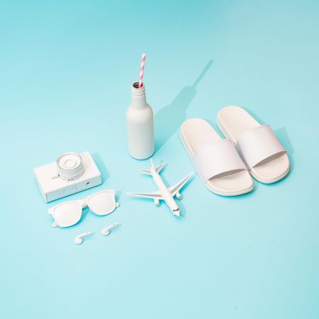 Flip flops, drinks, airplane and beach items on bright blue background