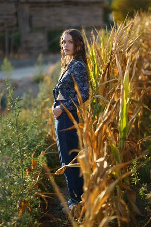 A young woman gracefully stands in a golden cornfield, enjoying the sunset and nature