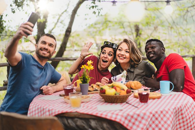 Multi-ethnic group of friends relaxing taking selfie at picnic table