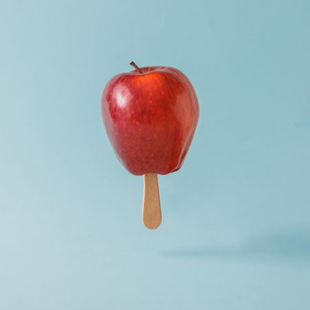 Red apple with ice cream stick on pastel blue background