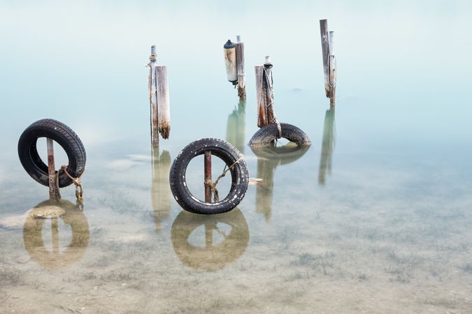 Old tires on sticks of former pier in water