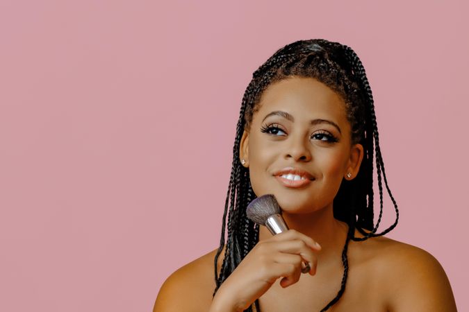 Thoughtful Black woman applying make up with brush to her cheek, copy space