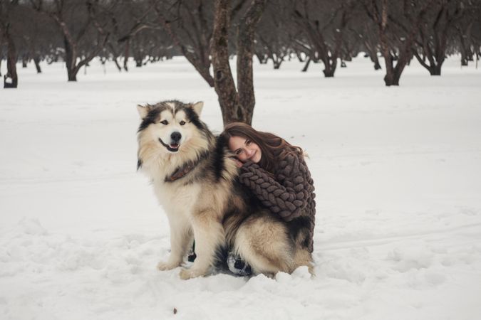 Woman hugging a husky dog on snow covered ground in woods