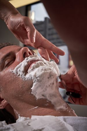 Faceless barber shaving beard of man in salon
