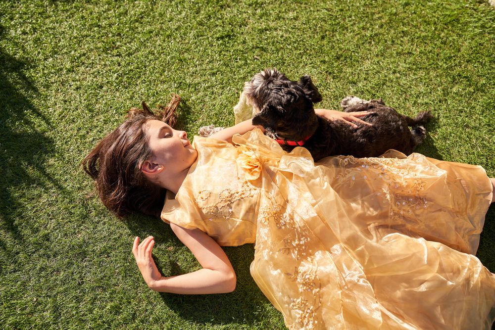 Happy girl in dress lying on green field with dog