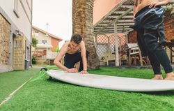 Surfer man in wetsuit waxing woman surfboard
