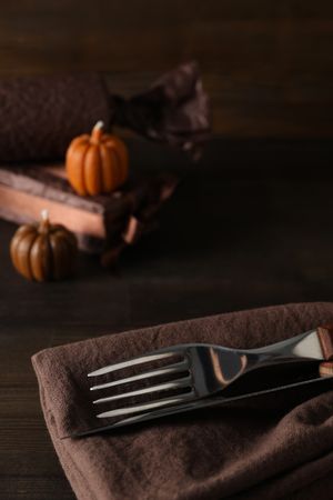 Cutlery on brown napkin and pumpkins on wooden background