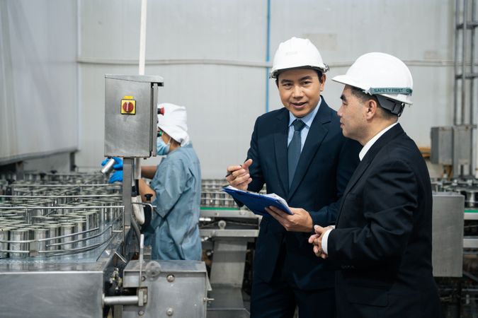 A businessman inspecting canned fish on conveyor belt at the factory