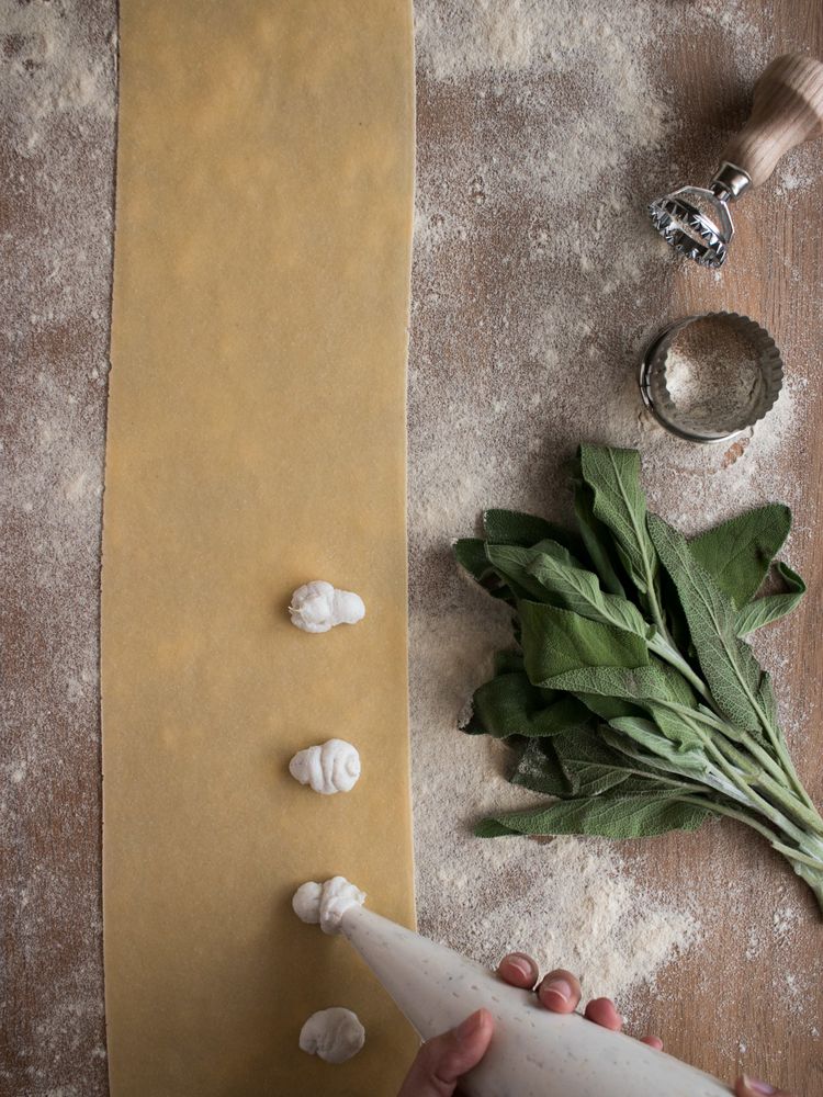 Crop hands squeezing stuffing on ravioli dough near sorrel
