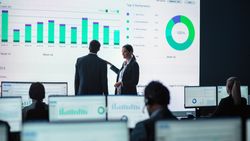 Business Professionals Analyze Performance Data on Large Screens in a Modern Office Setting, Focusing on Charts and Graphs to Drive Strategic Decisions.