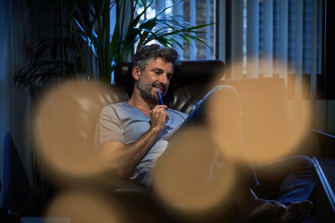 Thoughtful mature man sitting in armchair and writing notes