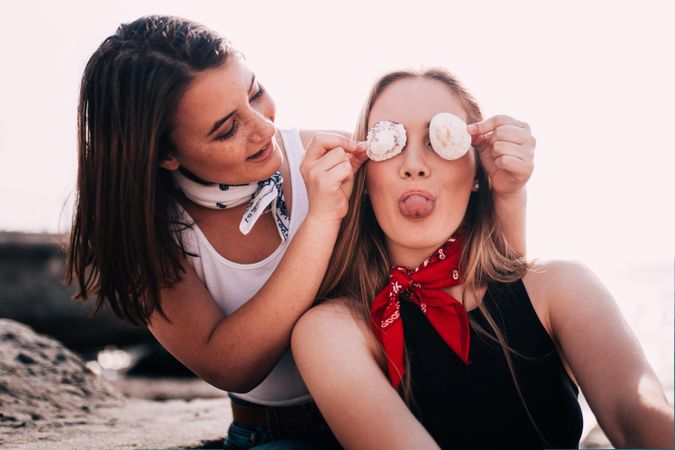 Young woman is playfully covering her friends eyes with seashells