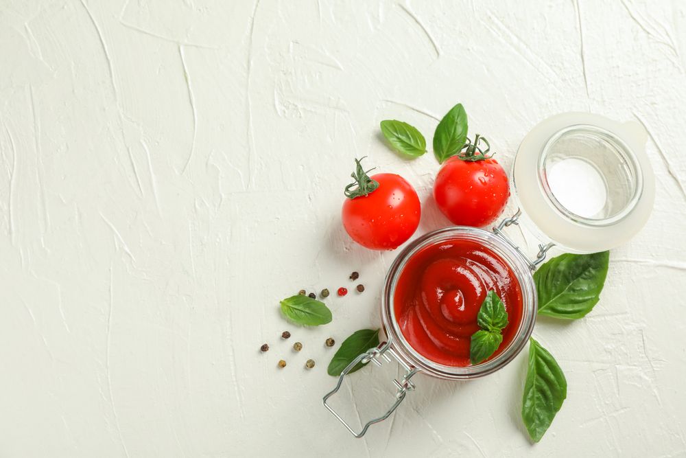 Flat lay composition with fresh tomatoes, basil, pepper and sauce in glass jar on plain background, space for text