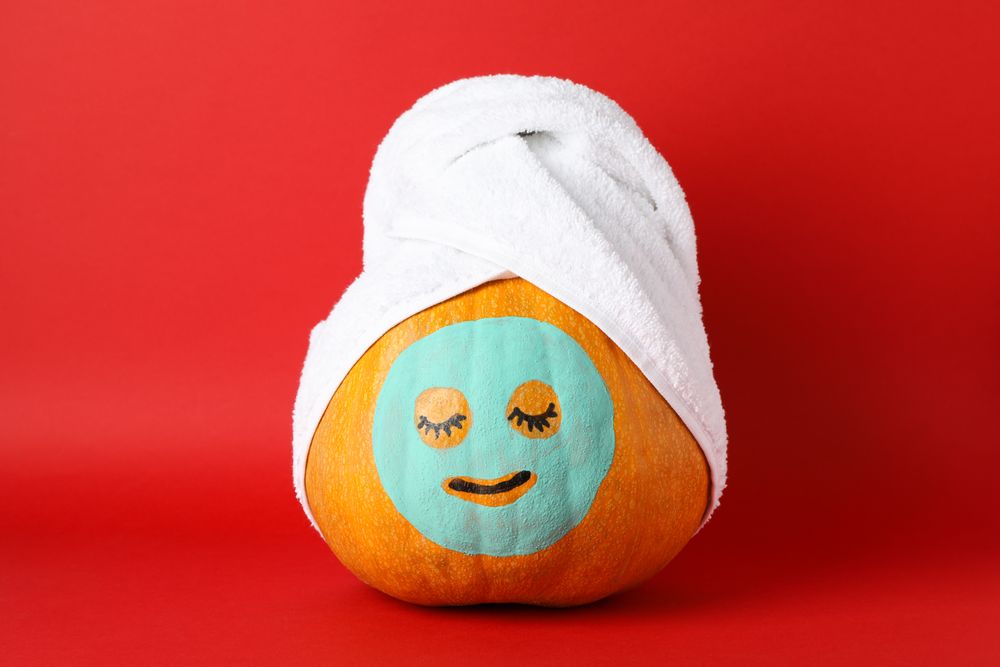 Pumpkin with facial mask and towel on red background, copy space